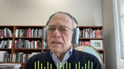  MIT President Emeritus Rafael Reif wears headphones in front of a bookshelf filled with books.